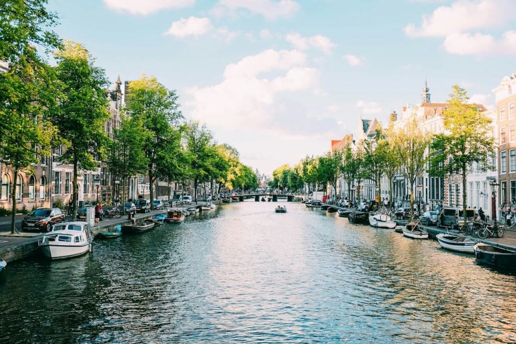 Boats moored along a canal lined with trees and historic buildings in Amsterdam