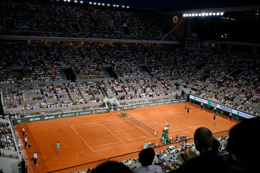 A crowded tennis stadium with a clay court at night.