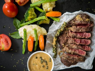 Grilled steak served with fresh vegetables and pepper sauce, presenting a colorful and appetizing meal.